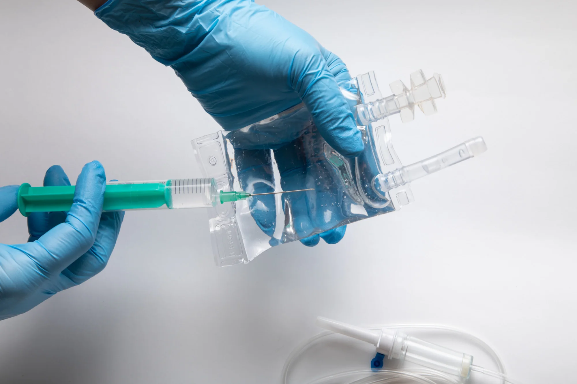 An IV fluid bag and infusion set being prepared by a gloved clinician